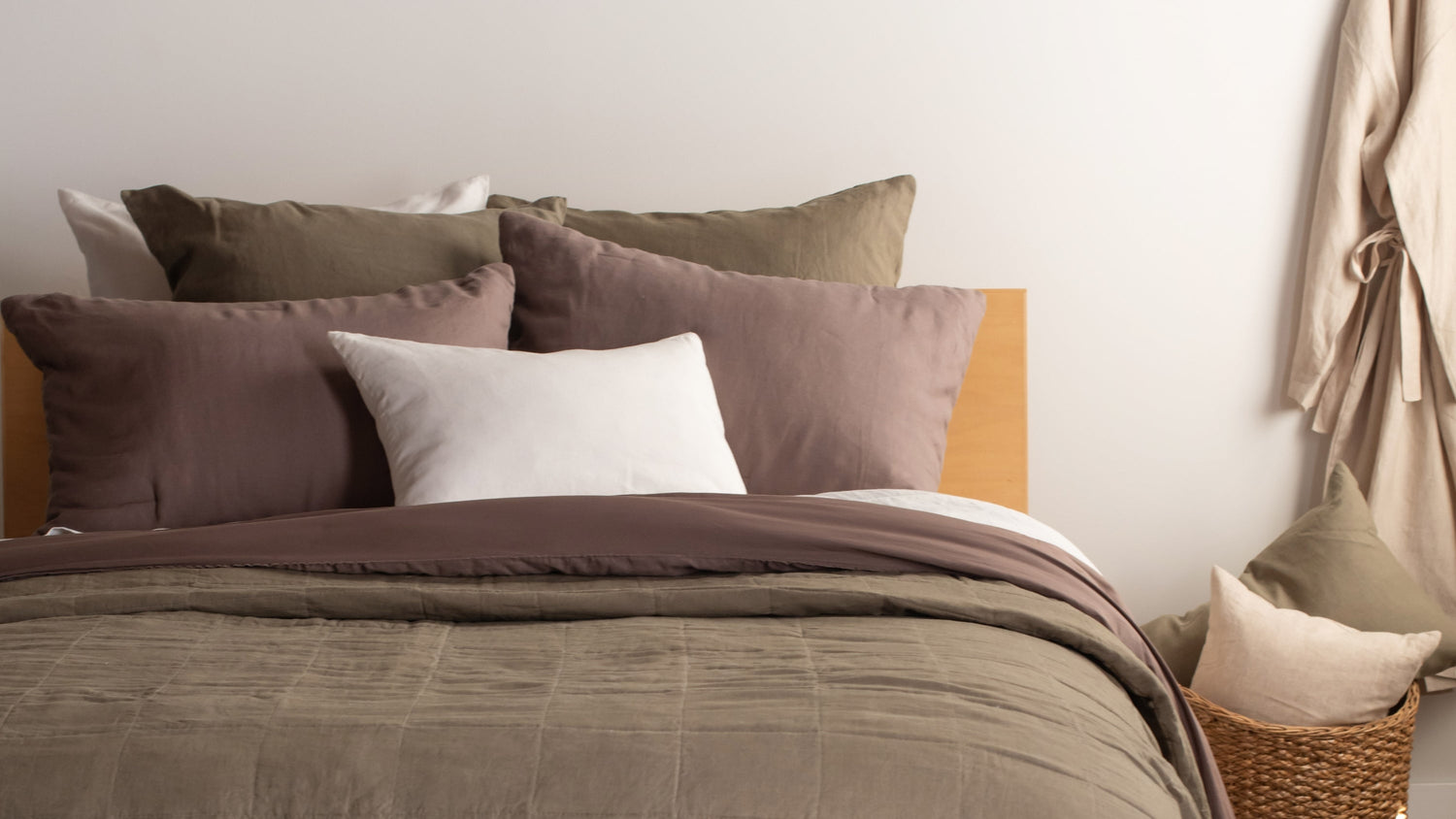 throw pillows piled on a bed with a quilt and comforter in green and brown